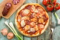 Rustic round pizza with salami. Cherry tomatoes, salami, garlic, leek and fork on background Royalty Free Stock Photo