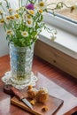 Rustic scene - old-fashionned glass vase with bouquet of chamomiles and wooden desk with mashrooms and knife on window background