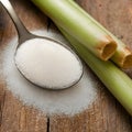 Rustic setup with granulated sugar spoon and sugarcane on wooden surface. Royalty Free Stock Photo