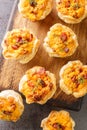 Rustic snack puff pastry muffins stuffed with eggs, cheese and ham close-up on a wooden board. Vertical top view