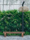 Rustic solid railway sleeper wooden bench on concrete floor with modern hand woven bamboo light on tropical green bush and bamboo