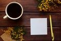 Rustic spring mock up with mimosa flowers, empty paper blank, yellow pen and cup of coffee. Top view, flat lay, copy space Royalty Free Stock Photo