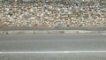 Rustic stone wall made of rocks and bricks. A sidewalk and asphalt road in front. Royalty Free Stock Photo