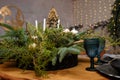 Rustic style Christmas festive table, blue glasses, plates and fresh thuja, fir branches bouquet with candles. Warm garland lights Royalty Free Stock Photo