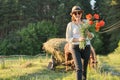 Rustic style, mature happy woman in hat with bouquets of poppies flowers walking along country road Royalty Free Stock Photo