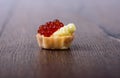Tartlet with red caviar and butter on a wooden background
