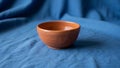 A rustic, terra cotta clay bowl sits on a solid blue fabric background. The bowl is small and Royalty Free Stock Photo
