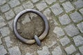 Rustic weathered iron mooring ring embedded in cobbled paving.