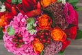 Rustic wedding bouquet with orange, crimson and bordeaux roses, poppy and other flowers and greens on wooden background