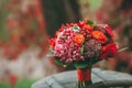Rustic wedding bouquet with red, orange and bordeaux roses, berries, and other greens on aged wooden logs. Artwork