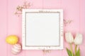 Rustic white wood frame with pastel Easter eggs and white spring tulip flowers. Top view against a pink wood background. Copy Royalty Free Stock Photo