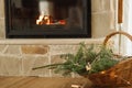 Rustic wicker basket with spruce branches, vintage bells and lights on background of burning fireplace. Festive christmas