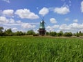 Rustic Windmill Amid Vibrant Green Fields Under a Blue Sky With Clouds Royalty Free Stock Photo