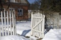 Rustic winter landscape with a wooden fence and a snow-covered little house behind it. A sunny day with a blue clear sky Royalty Free Stock Photo