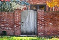 Rustic wooden arched garden fence in brick wall in autumn with colored leaves and brick house with colorful fall foliage reflected