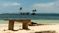 Rustic wooden bench on a sandy tropical beach overlooking a blue ocean and rocky island with palm trees on Bocas Del Toro, Panama
