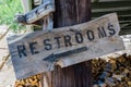 Rustic wooden board sign on a post with black writing and arrow pointing to public restroom