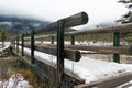 A rustic wooden bridge spans a gentle stream in a wintry forest setting Royalty Free Stock Photo