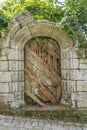 Rustic wooden door set in an old stone arch and wall with green vegetation Royalty Free Stock Photo