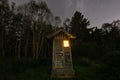 A rustic wooden outhouse with a warm light inside, under a starry night sky in a dark forest clearing Royalty Free Stock Photo