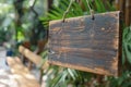 Rustic wooden sign hangs by rope, blank inviting customization against verdant background. Botanical garden setting with