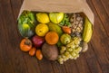 A rustic wooden table with a paper bag full of lots of freshly picked fresh fruit. Many vitamins together on a wooden table