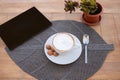 A rustic wooden table ready for the breakfast with a hot cappuccino, and some little cookies. Black tablet on the table