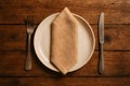 A rustic wooden table is set with a simple white plate, a folded napkin, a knife and a fork Royalty Free Stock Photo
