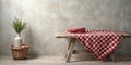 Rustic wooden table setting with red and white checkered tablecloth, a vase of greenery, and a wicker basket against a textured Royalty Free Stock Photo