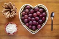 Close-up view from above of white heart-shaped plate full of red grapes, cream and biscuits. Wooden background