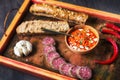 Rustic wooden tray with simple Balkan foods - ajvar spread, bread, meat, garlic and chilli peppers