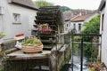 Rustic wooden waterwheel next to baskets of flowers with water flowing by. Crecy-la-Chapelle, France.