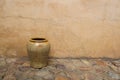 Rustic yellow clay vase on cobble stone floor, pavement against shabby ochre textured wall, house facade. Old French