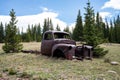 Rusty abandoned truck wreck in the field by green trees