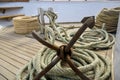 Rusty anchor with coiled rope lies on wooden deck of yacht. Auxiliary yacht equipment. Copy space. Close-up. Royalty Free Stock Photo