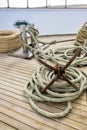 Rusty anchor with coiled rope lies on wooden deck of yacht. Auxiliary yacht equipment. Copy space. Close-up. Royalty Free Stock Photo