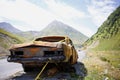 A rusty, burnt-out car with no taillights on the road in the mountains. Royalty Free Stock Photo