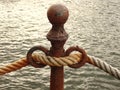 A rusty cast metal bollard with a gross hawser.