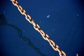 Rusty chain illuminated by the rays of the sun and its tortuous shadow reflected in the blue water of the sea Royalty Free Stock Photo