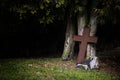 Rusty cross made of metal leaning against old tree trunks in shadow under the tops, religious christian symbol for death, Good Fr