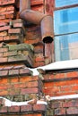 Rusty drain pipe along window corner on red brick wall, snow on window sill