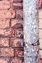 Rusty drain pipe with coiled wire on red brick wall