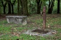 A rusty fountain next to a stone bench in a park on a cloudy day