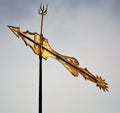 Rusty, gold weather vane against a cloudy blue sky