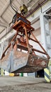 Rusty grab bucket or clamshell hanging on crane in empty industrial plant