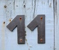 A rusty grey metal house number plaque, fixed on a fence, showing the number eleven