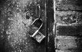 On the rusty handle of an old metal door hangs a metal open lock. Black and white Royalty Free Stock Photo