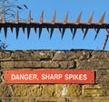 Rusty iron sharp spikes on the top of an old stone wall with a red danger sign against a blue sky Royalty Free Stock Photo