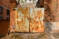 Rusty locked steel gate of deserted 1970s` red brick workshop