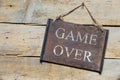 Rusty metal sign on wooden table, text game over